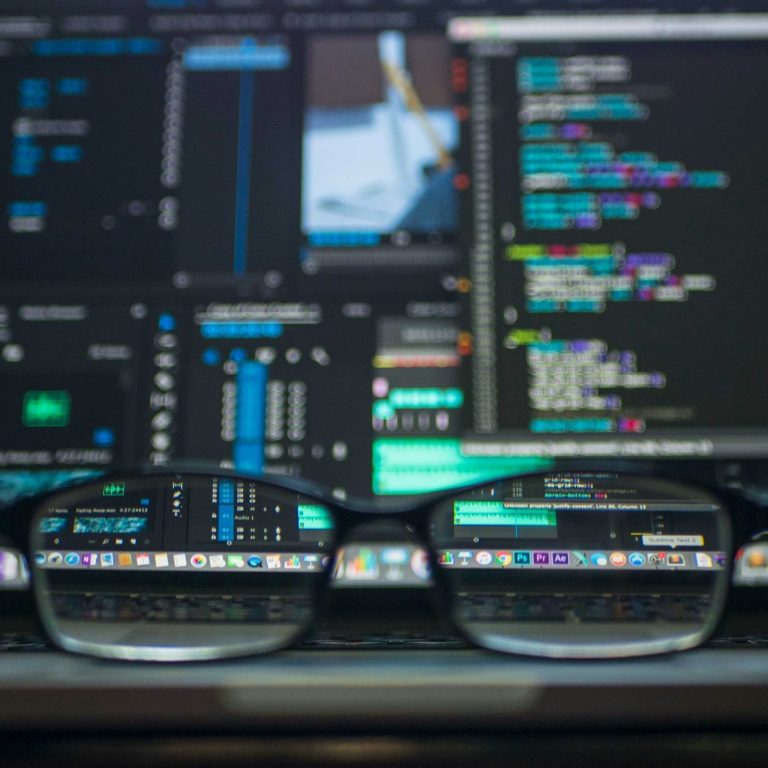 Close-up of glasses in front of a computer screen displaying code and software interface.